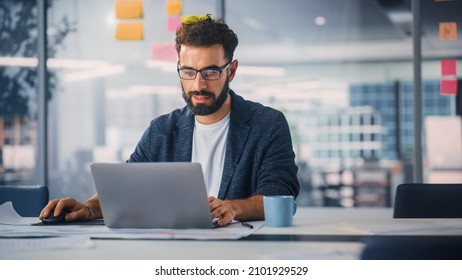 Modern Office: Portrait of Young Stylish Businessman Wearing Glasses Works on Laptop, Does Data Analysis, Website Design, Creative Developemnt. Digital Entrepreneur Works on e-Commerce Startup Project