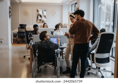 A modern office scene captures a dynamic team including a professional in a wheelchair discussing ideas and collaborating in a bright workspace. - Powered by Shutterstock