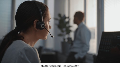 In modern office: Serious female stock exchange trader in headset works on computer. Professional stockbroker communicates with business client, monitors shares and stock market. Finance and trading. - Powered by Shutterstock