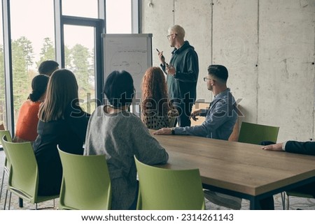 In a modern office setting, a group of business professionals attentively listens to a captivating presentation delivered by their young colleagues, showcasing their teamwork, engagement, and