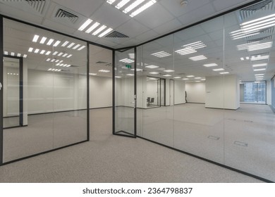 Modern office space with light walls and floor, and glass partitions.