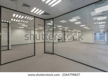 Modern office space with light walls and floor, and glass partitions.