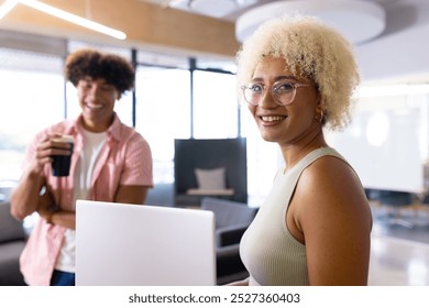 In modern office, two biracial coworkers holding coffee, laughing together. Both with curly hair, enjoying lively blue background and vibrant office atmosphere, unaltered - Powered by Shutterstock