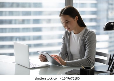 Modern office worker. Concentrated focused young businesswoman employee manager doing electronic paperwork at workplace using devices comparing checking synchronizing data at pad and laptop memory