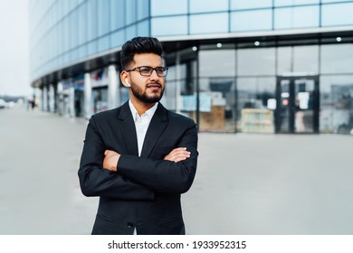 A Modern Office Worker, An Indian Man, A Bank Employee In A Black Suit, Behind A Large Wooden Building.