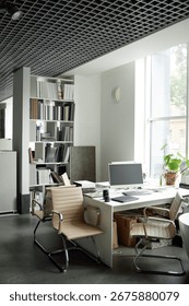 Modern office workspace featuring empty chairs surrounding desk with computer monitor, bookshelves filled with documents in background, large window letting in natural light, no people visible