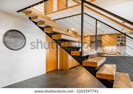 Modern open concept home interior kitchen with floating stairs and grey slate floors beamed ceiling and wood cabinets