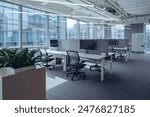 The modern open-plan office with a clean, organized layout. The workspace features rows of individual desks equipped with computers and ergonomic office chairs, separated by privacy screens.