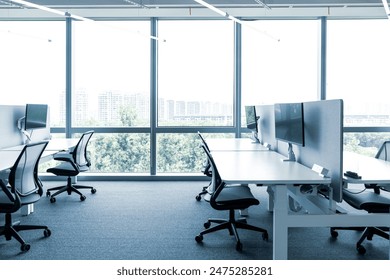 The modern open-plan office with a clean, organized layout. The workspace features rows of individual desks equipped with computers and ergonomic office chairs, separated by privacy screens. - Powered by Shutterstock