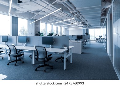 The modern open-plan office with a clean, organized layout. The workspace features rows of individual desks equipped with computers and ergonomic office chairs, separated by privacy screens.