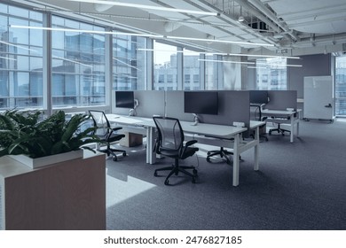 The modern open-plan office with a clean, organized layout. The workspace features rows of individual desks equipped with computers and ergonomic office chairs, separated by privacy screens. - Powered by Shutterstock