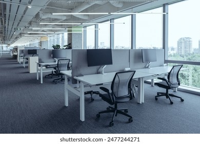 The modern open-plan office with a clean, organized layout. The workspace features rows of individual desks equipped with computers and ergonomic office chairs, separated by privacy screens.