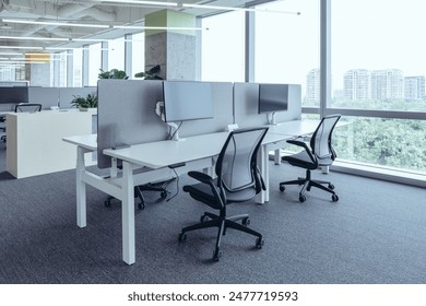 The modern open-plan office with a clean, organized layout. The workspace features rows of individual desks equipped with computers and ergonomic office chairs, separated by privacy screens. - Powered by Shutterstock