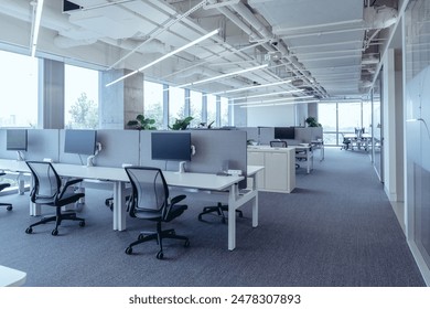 The modern open-plan office with a clean, organized layout. The workspace features rows of individual desks equipped with computers and ergonomic office chairs, separated by privacy screens. - Powered by Shutterstock