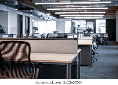 Modern open-plan office space featuring ergonomic workstations equipped with adjustable chairs and computer monitors mounted on desk arms. The design emphasizes clean lines and a neutral color palette