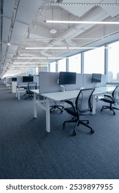 Modern open-plan office space featuring ergonomic workstations equipped with adjustable chairs and computer monitors mounted on desk arms.