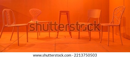 Modern orange stools and chairs of various designs on an orange painted floor and wall background.