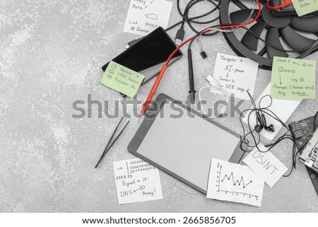 Modern OSINT setup with smartphone, tablet, probes, cables and sticky notes with investigative hints symbolising press freedom and data analysis. Grey concrete background, flat lay, top view
