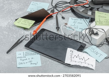 Modern OSINT setup with smartphone, tablet, probes, cables and sticky notes with investigative hints symbolising press freedom and data analysis. Grey concrete background, copy space