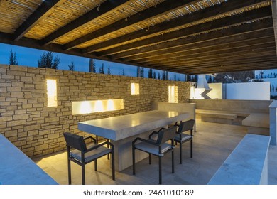 Modern Outdoor Dining Area With Stone Table and Warm Lighting at Twilight.A long, sleek dining table paired with comfortable chairs under a rustic thatched roof.  - Powered by Shutterstock