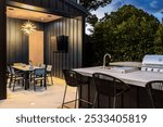 Modern outdoor kitchen and dining area with sleek furniture, grill, and stylish lighting, surrounded by lush greenery.