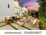 Modern outdoor patio with cozy seating and fire pit, set against a vibrant sunset sky, showcasing contemporary design and lush greenery.