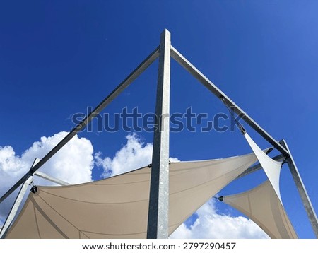a modern outdoor shading structure featuring multiple white tensile fabric canopies stretched taut over a framework of galvanized steel beams and vertical posts. The composition emphasizes clean lines, contemporary architectural design
