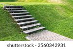 Modern outdoor staircase on a green grassy slope, leading to a paved path. Minimalist design, natural setting, landscaping concept