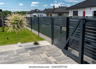 A modern panel fence in anthracite color, a visible sliding gate to the garage and a wicket with a letterbox.