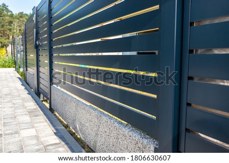 Modern panel fencing in anthracite color, visible spans and a wicket, forest in the background.