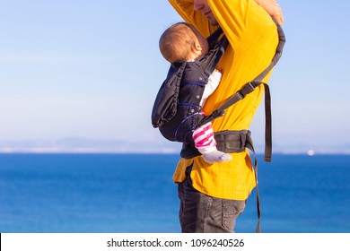 Modern Parenting. Dad With Baby Daughter In  A Carrier In The Beach