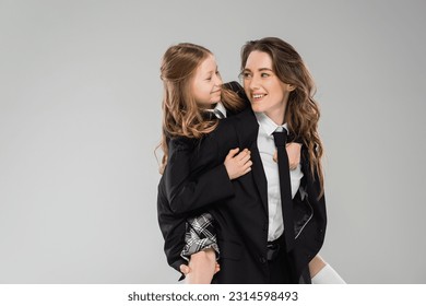 modern parenting, happy mother piggybacking her daughter, working mom in business attire and schoolgirl in uniform on grey background in studio, fashionable family, having fun - Powered by Shutterstock