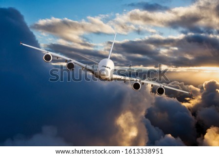 Modern passenger 4-engine plane in flight. Aircraft flies on a high altitude over the storm clouds during the sunset. Front view and right roll of the aircraft.