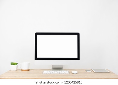 Modern PC Monitor and white screen, mouse, keyboard and some stuff on the wooden table. White background and copy space. Business or Work space theme
