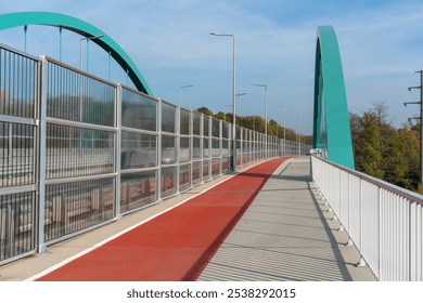 Modern pedestrian and bike bridge with red lane and turquoise arch structure on clear sunny day. Concept of sustainable urban design, active commuting, and infrastructure for cyclists and pedestrians. - Powered by Shutterstock