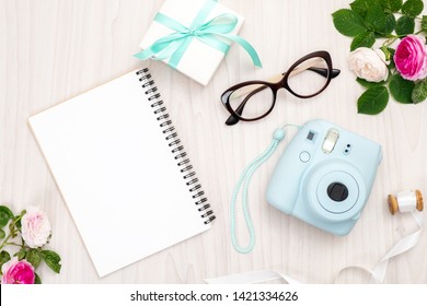 Modern polaroid camera, gift box, glasses, feminine accessories, roses on wooden background. Top view, tender minimal flat lay style composition. Women desk, fashion blogger, beauty technology