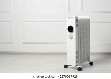 Modern portable electric heater on floor near white wall indoors, space for text