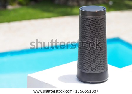 Modern portable music speaker with voice assistant near the swimming pool.