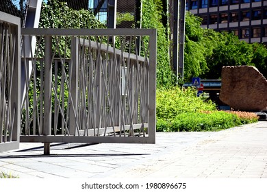 Modern Powder Coated Aluminum Fence And Gate. Light Stone Pavement. Office Bulding In The Background. Streetscape. Lush Green Hedge And Tree Along The Sidewalk. Urban Scene. Diminishing Perspective