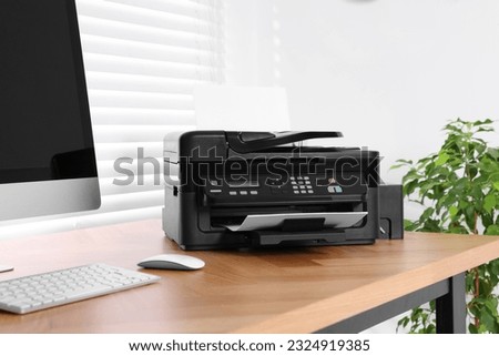 Modern printer with paper near computer on wooden table in home office