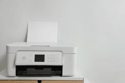 Modern Printer With Paper On Table Near White Wall, Space For Text