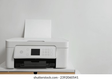 Impresora moderna con papel sobre mesa cerca de la pared blanca, espacio para texto