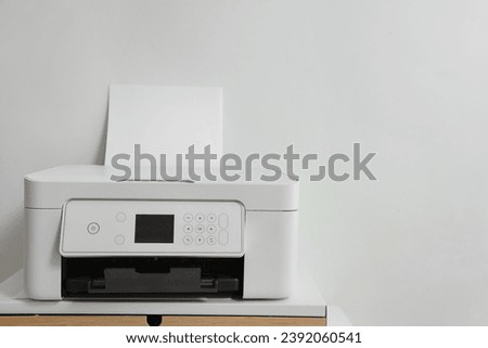 Modern printer with paper on table near white wall, space for text