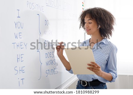 Modern profession is online teacher. Friendly african american girl in wireless headphones writes on blackboard english rules, copy space