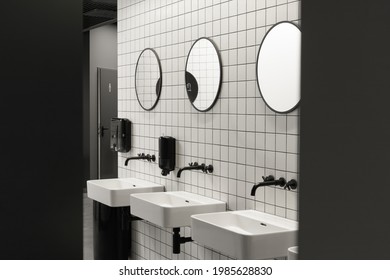 Modern public restroom minimal interior with metro style white tiles, round mirrors, black ceiling
