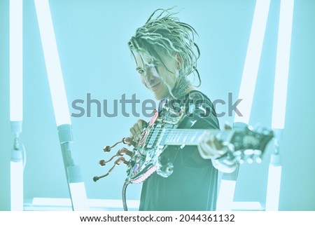 Modern punk rock music. Portrait of an expressive punk rock musician with dreadlocks posing with an electric guitar among neon lamps. Youth alternative culture. Cyberpunk and space style.