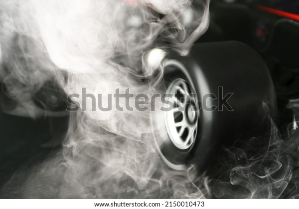 Modern racing car with smoke from under wheels on\
dark background, closeup