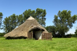 Modern Reconstruction Of A Bronze Or Iron Age Roundhouse. Typically The Walls Were Made Of Either Stone Or Of Wooden Posts Joined By Wattle And Daub Panels, Topped With A Conical Thatched Roof. 
