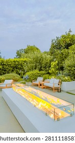 Modern rectangular glass fire pit with bright orange flames glowing in a luxury outdoor patio setting during the soft evening
