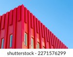 Modern red architectural office building. Metal sheets covering the exterior of the structure. Modern futuristic style building. Clear sky at the background. Unique building.